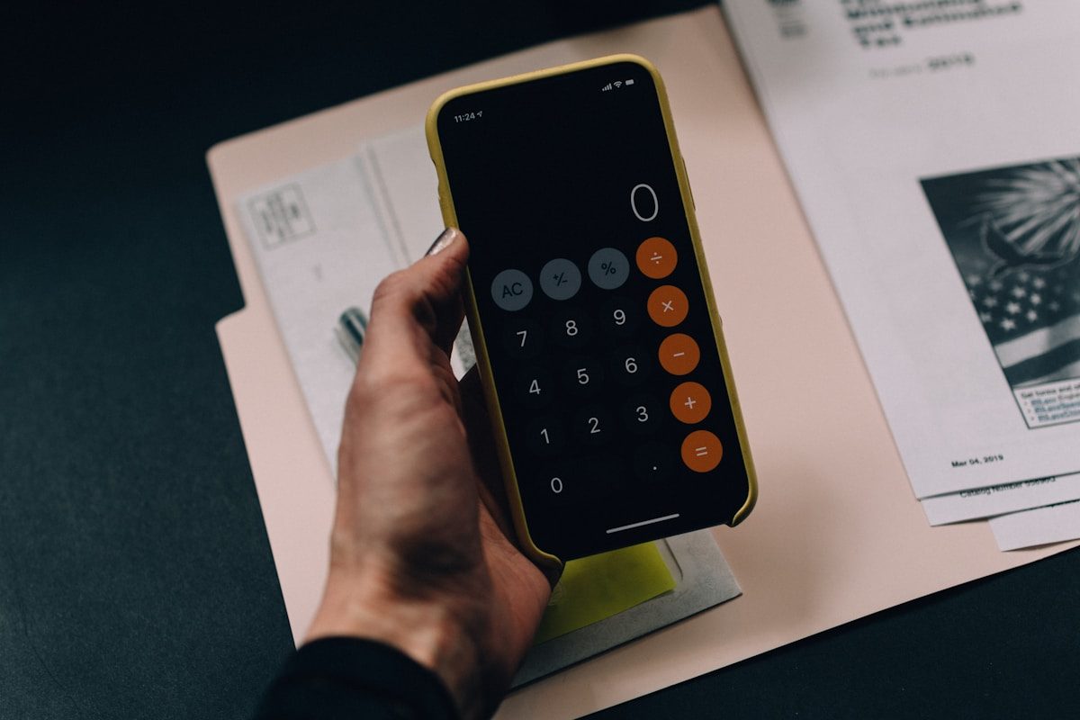 Mano sosteniendo el teléfono con la calculadora abierta sobre documentos